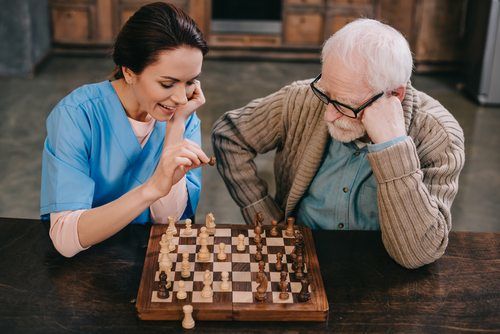 A nurse and a senior man playing chess together