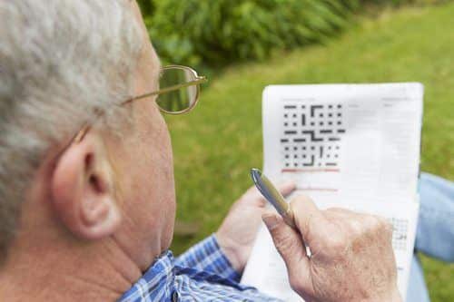 Senior Man Doing Crossword Puzzle In Garden