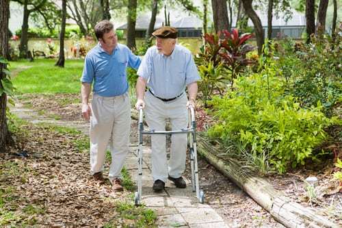 Middle-aged man and senior man with a walker strolling in garden.