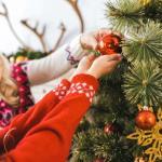 Senior woman helping younger girl hang ornament on Christmas tree