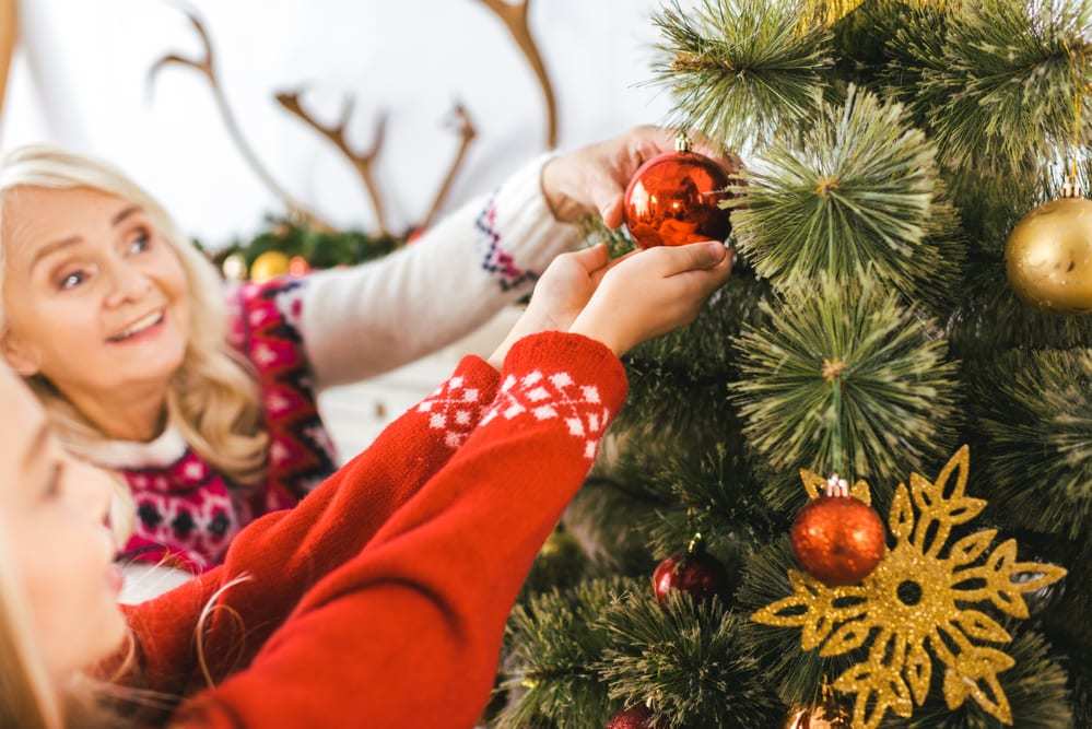 Senior woman helping younger girl hang ornament on Christmas tree