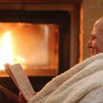 Senior man relaxing by fireplace with book and blanket