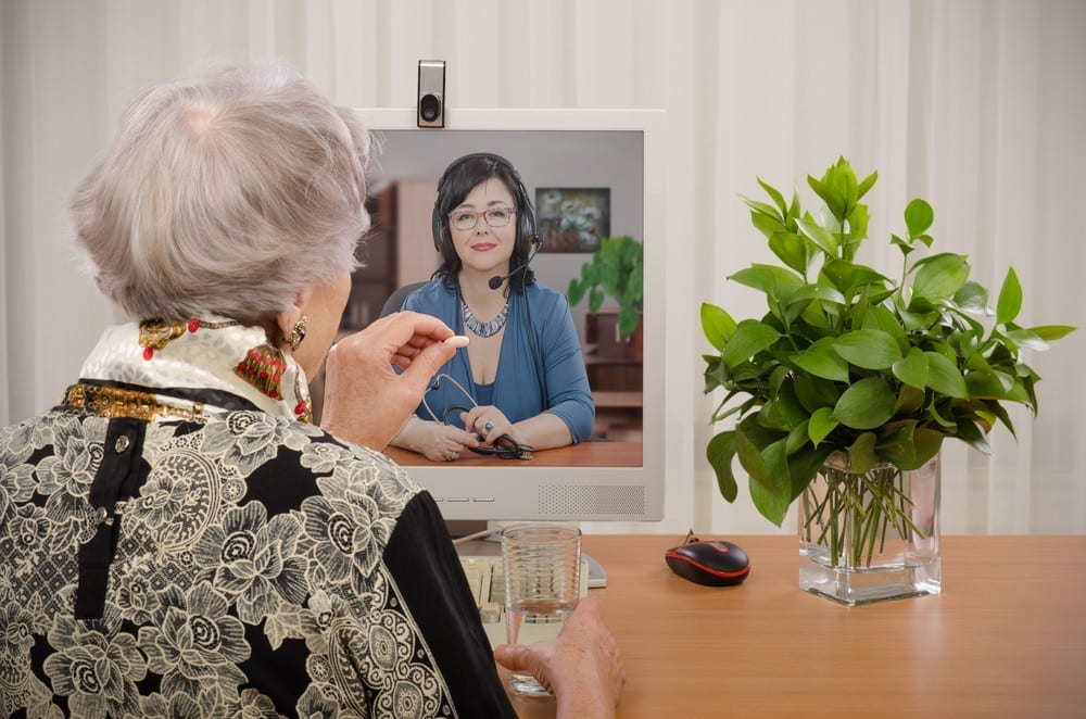 Senior woman taking pill in front of virtual doctor