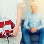 Child holding red present behind back, ready to present to grandfather in background