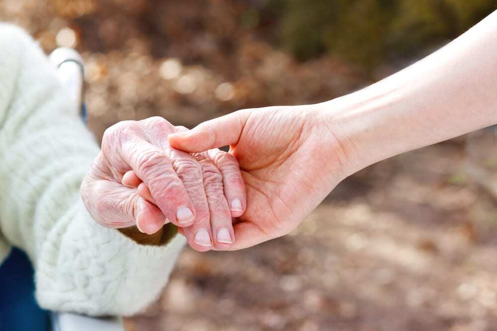 Close-up of young adult holding the hand of a senior outside