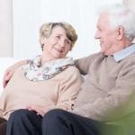 Senior couple sitting on couch, smiling at each other