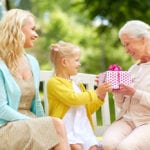 Smiling daughter and granddaughter giving grandma a gift on bench outside