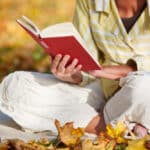 Close-up of senior reading cross-legged on autumn leaves