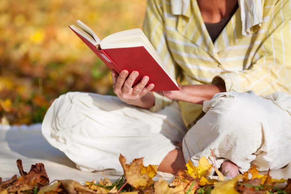 Close-up of senior reading cross-legged on autumn leaves