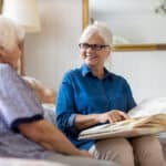Older woman looking at photo album with senior woman, smiling