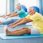 Seniro man and woman stretching to touch their toes in gym