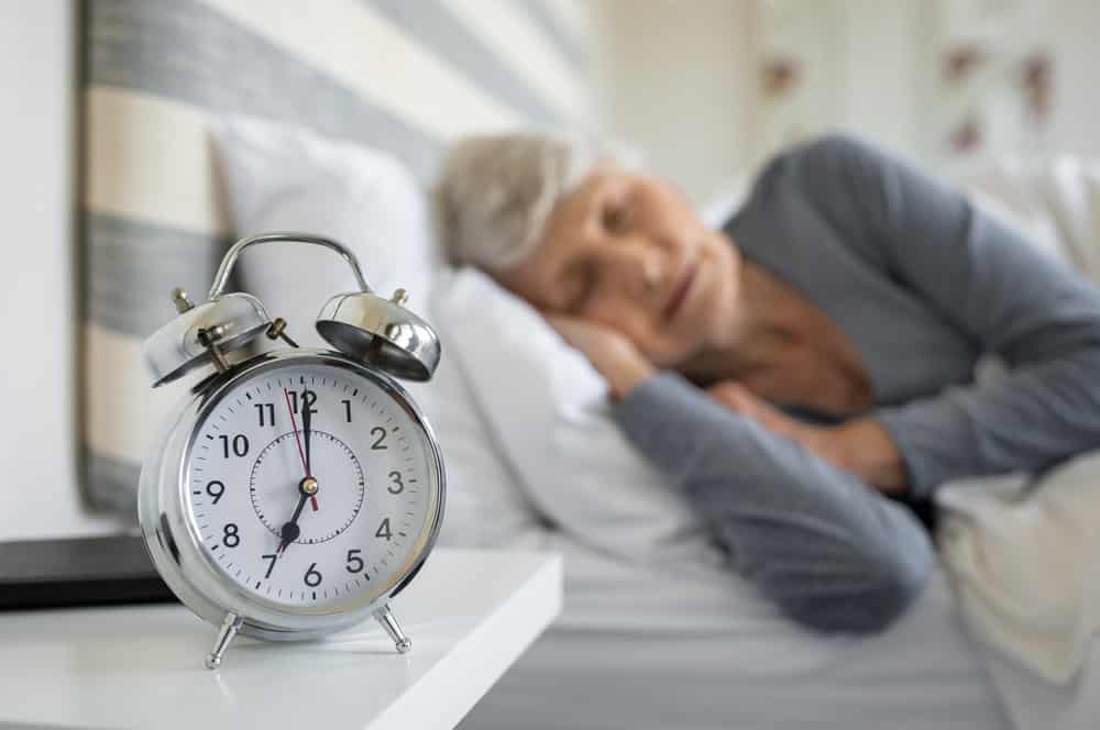 Senior woman sleeping in background, alarm clock in foreground