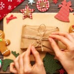Hands tying twine into a bow to wrap a gift, crafty items and gingerbread cookies surrounding