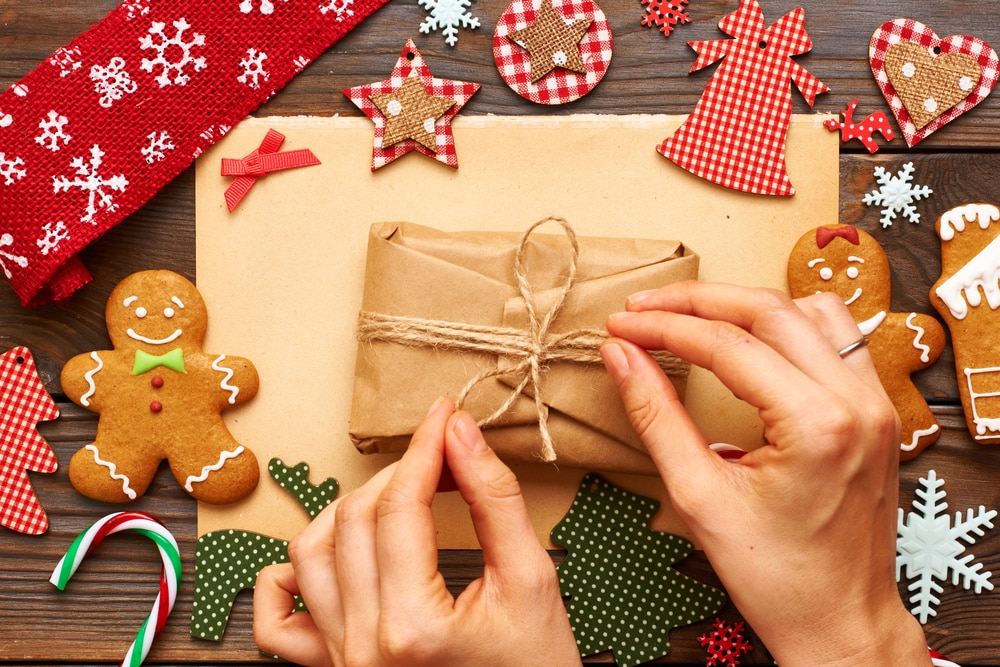 Hands tying twine into a bow to wrap a gift, crafty items and gingerbread cookies surrounding
