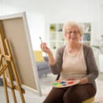 Senior woman holding a palette and painting indoors
