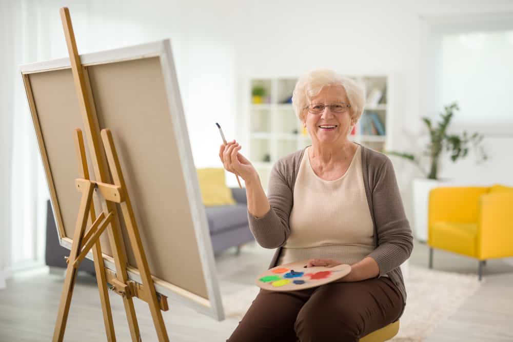 Senior woman holding a palette and painting indoors
