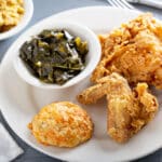 Fried chicken with a biscuit and collard greens on dinner plate