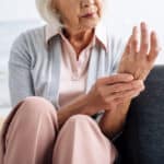 Cropped view of senior woman on couch holding her wrist with other hand