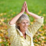 senior woman performing yoga in the park in fall
