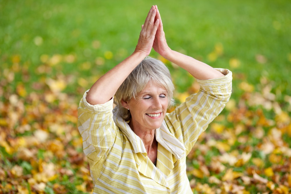 senior woman performing yoga in the park in fall