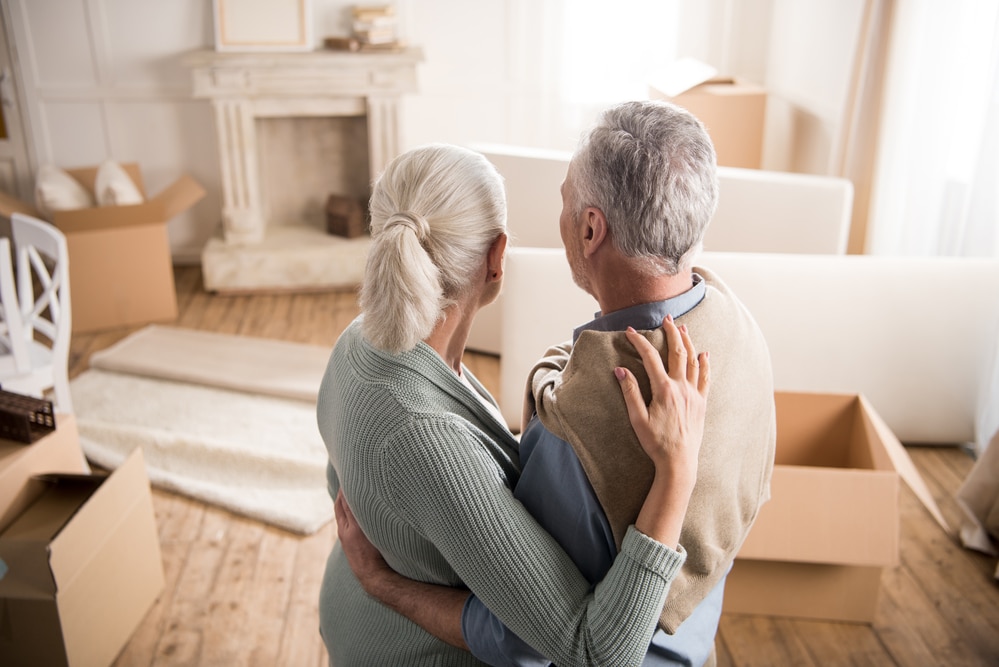 Senior couple holding each other, looking at apartment filled with boxes