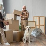Senior couple packing their home into cardboard boxes, dog looking at camera