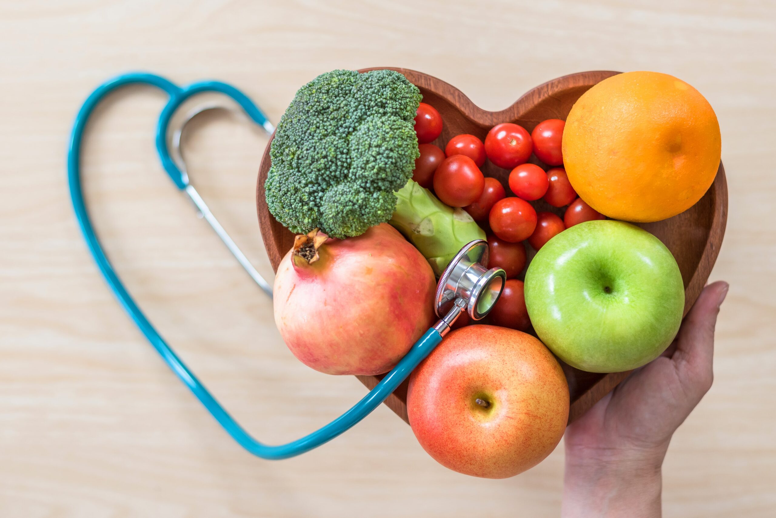 Fruits and veggies in heart shaped bowl, beside stethoscope in heart shape