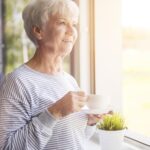 Senior woman gazing happily out window, holding cup of coffee