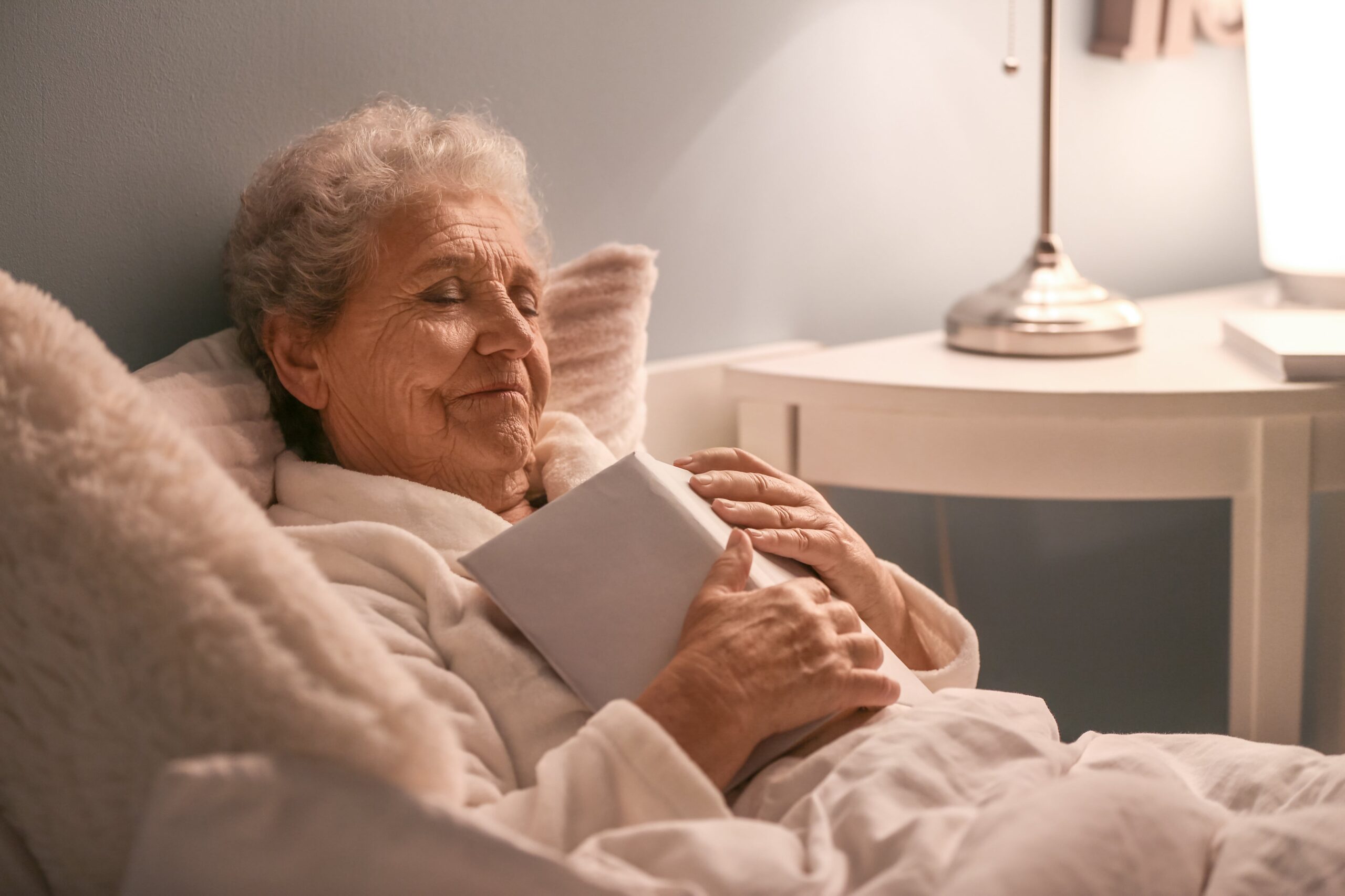 Senior woman relaxed in bed after reading, book on chest